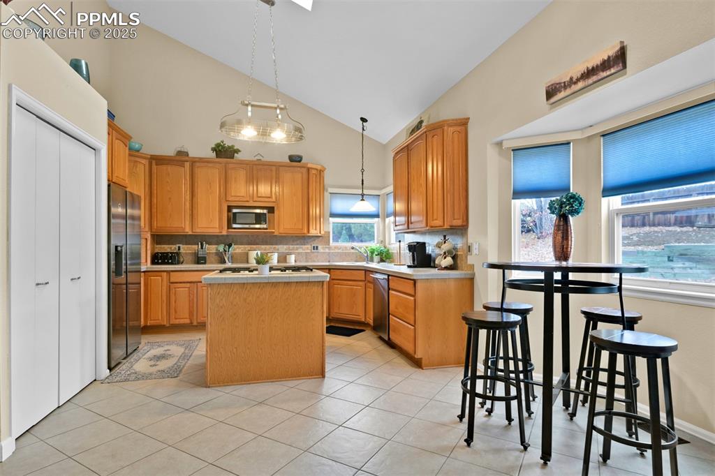 Image 11 of 50: Kitchen featuring a kitchen island, high vaulted ceiling, backsplash, light