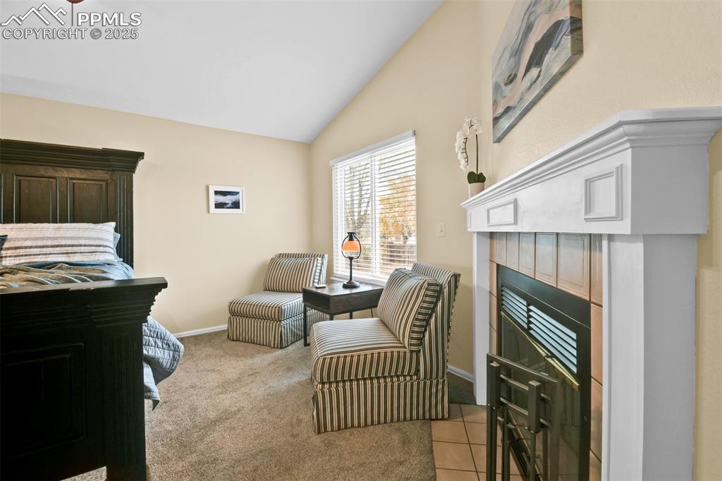 Image 27 of 50: Bedroom with lofted ceiling, light carpet, a tile fireplace, and light tile