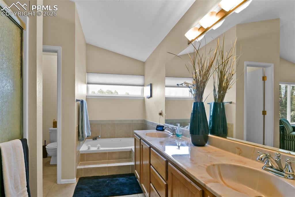 Image 30 of 50: Bathroom featuring vaulted ceiling, double vanity, light tile patterned flo