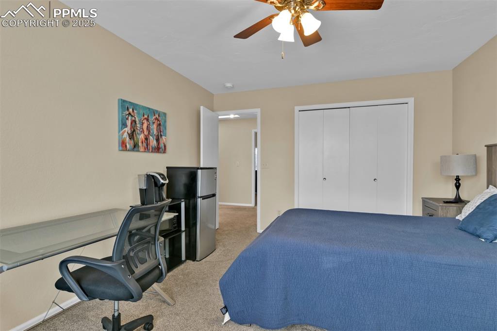 Image 32 of 50: Carpeted bedroom with freestanding refrigerator, a ceiling fan, and a close
