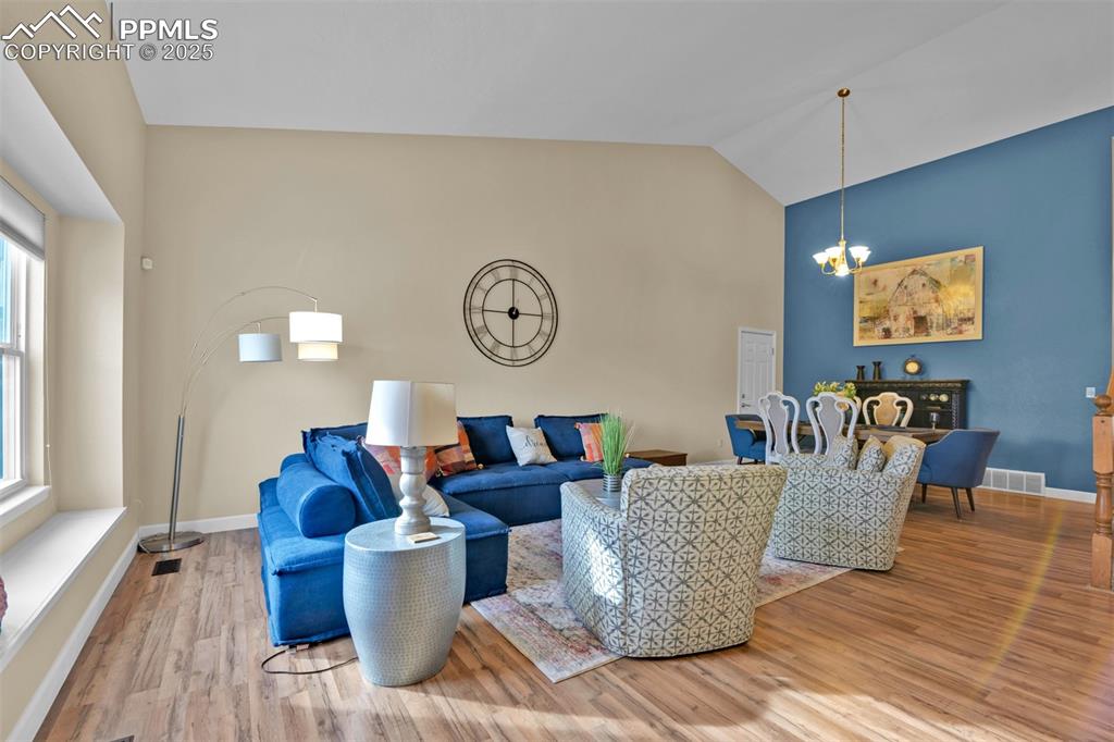 Image 4 of 50: Living room with wood finished floors, a chandelier, and vaulted ceiling