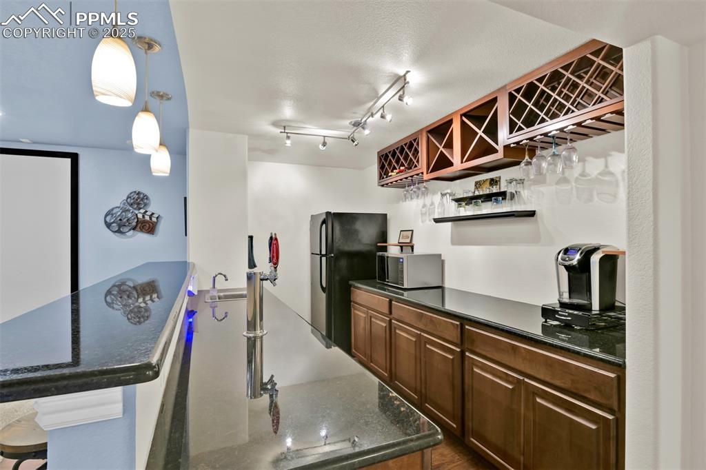 Image 41 of 50: Wetbar with a breakfast bar area, open shelves, dark stone counters, and fr