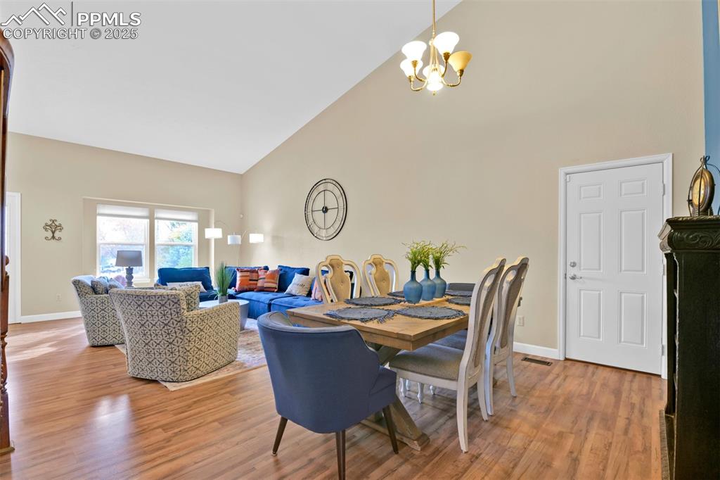Image 8 of 50: Dining area with high vaulted ceiling, light wood-style flooring, and a cha