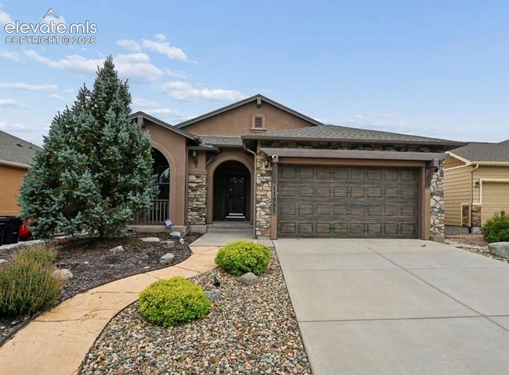 Caption: Stucco exterior with stone accents, arched entryway, a concrete driveway, and an attached garage wit