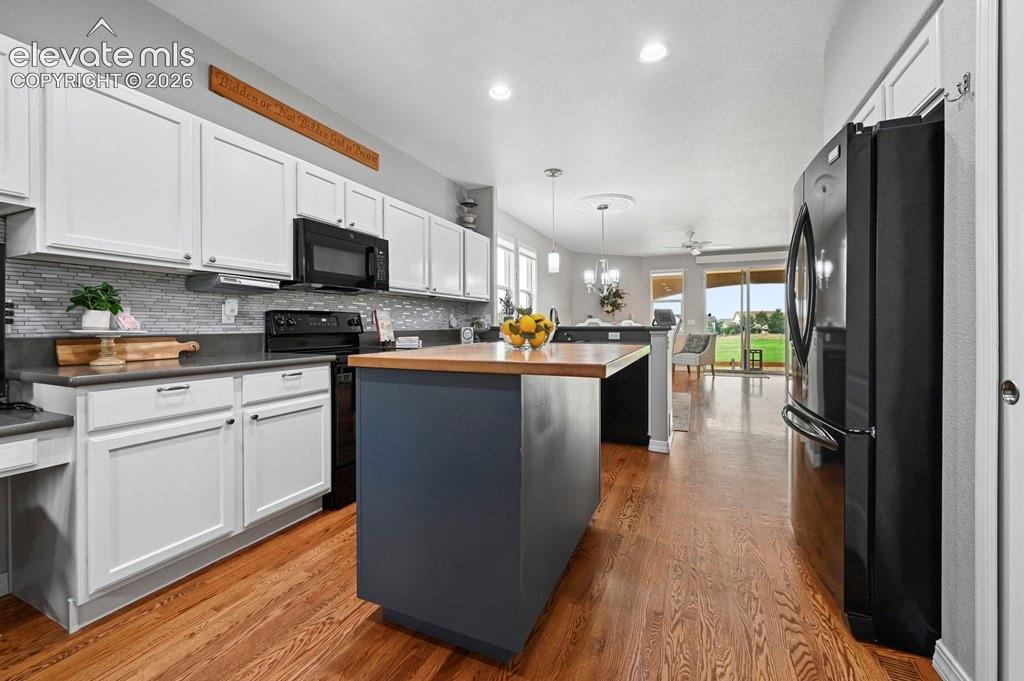 Image 12 of 39: Kitchen featuring white cabinetry, a tiled backsplash, and wood-finish floo