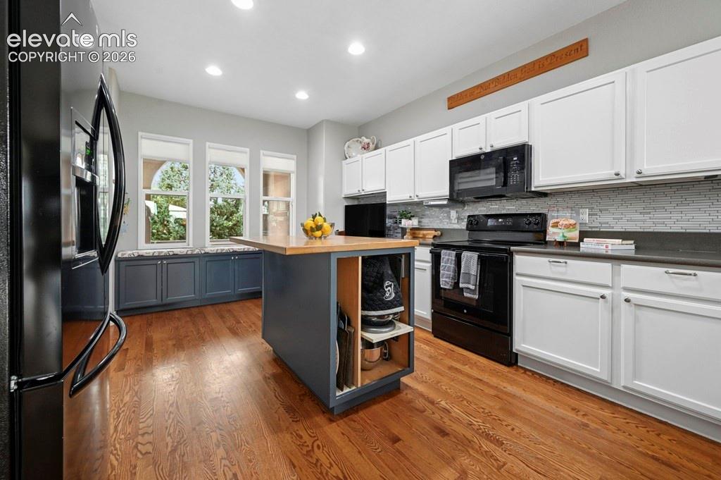 Image 9 of 39: Hardwood flooring, kitchen island with wood-finish countertop, white upper 
