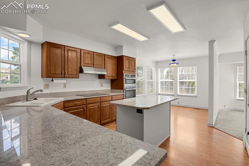 Image 11 of 50: This kitchen features granite countertops, wood cabinetry, and an island wi