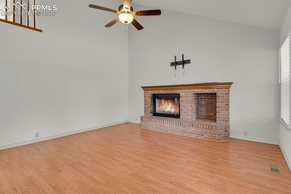 Image 15 of 50: Spacious living area featuring a brick fireplace, vaulted ceilings, and lig
