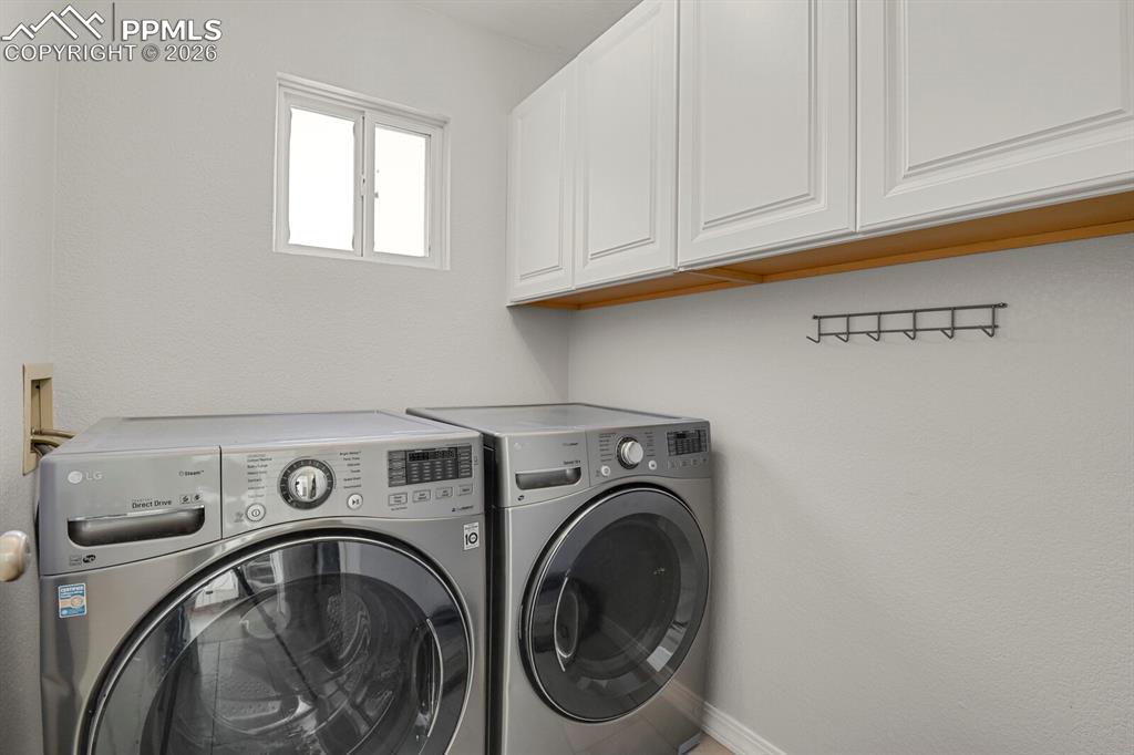 Image 20 of 50: This laundry area features white upper cabinetry, a window providing natura