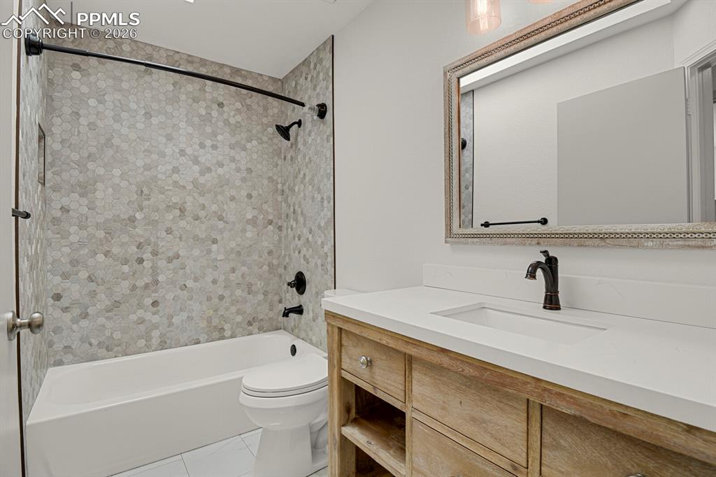 Image 31 of 50: Bathroom with a white bathtub, hexagon tiled shower surround, and dark-tone