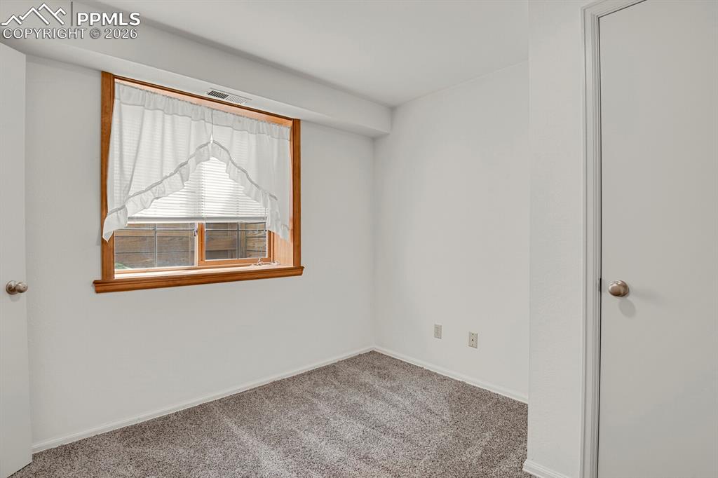 Image 37 of 50: The room features light gray carpeting, white walls, and a window with wood