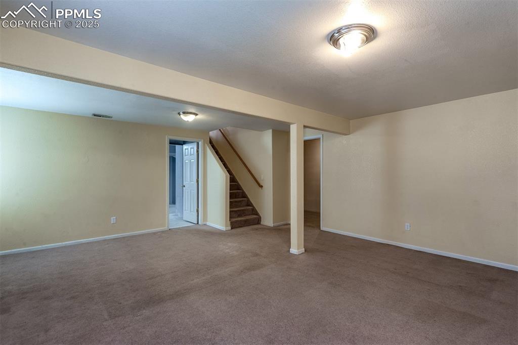 Image 18 of 31: Finished basement with visible vents, carpet floors, baseboards, and stairw