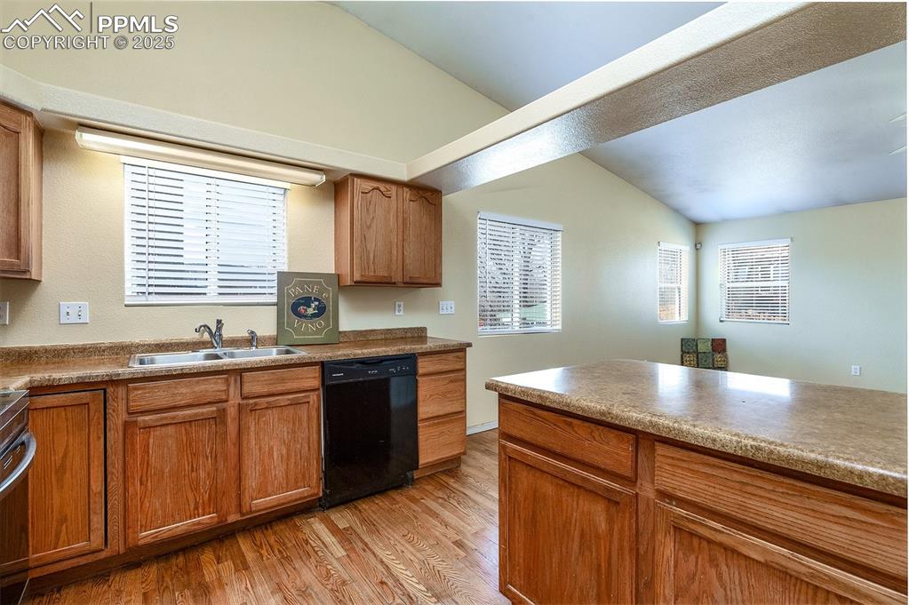 Image 6 of 31: Kitchen with light wood-type flooring, brown cabinets, a sink, black dishwa