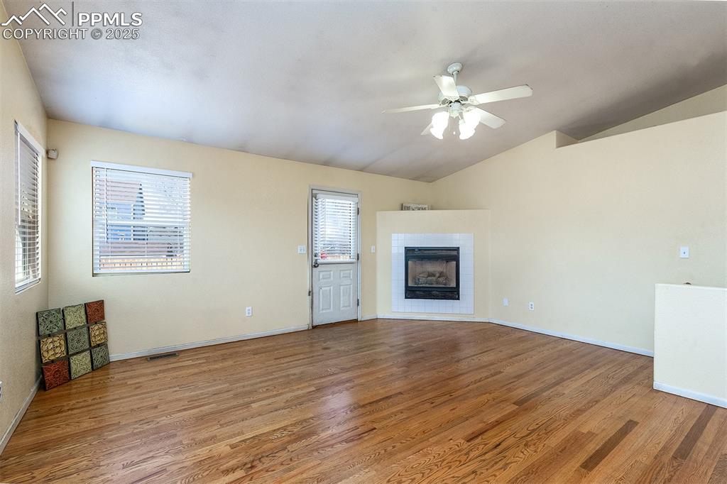 Image 8 of 31: Unfurnished living room featuring baseboards, a tiled fireplace, vaulted ce