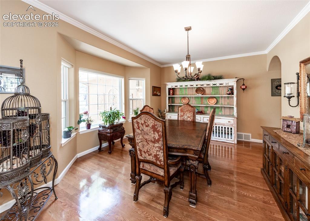 Image 17 of 50: Dining area featuring a bay window, crown molding, wood-finish flooring, an