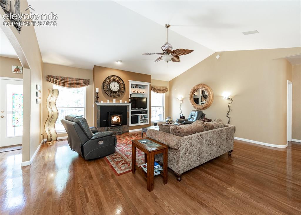 Image 21 of 50: Living area featuring wood-finish flooring, vaulted ceilings, and a firepla