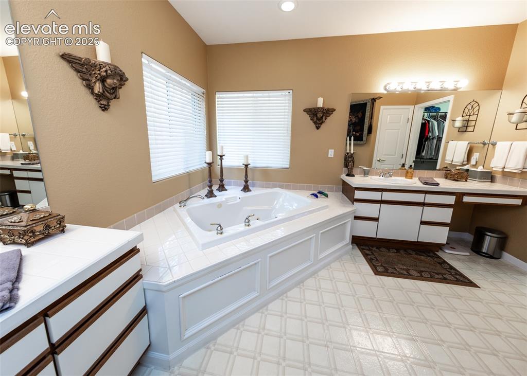 Image 24 of 50: Bathroom featuring a built-in jetted tub with tiled surround, dual windows