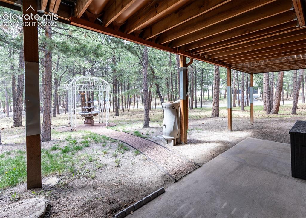 Image 47 of 50: Covered patio with concrete flooring, wood beam ceiling, and structural woo