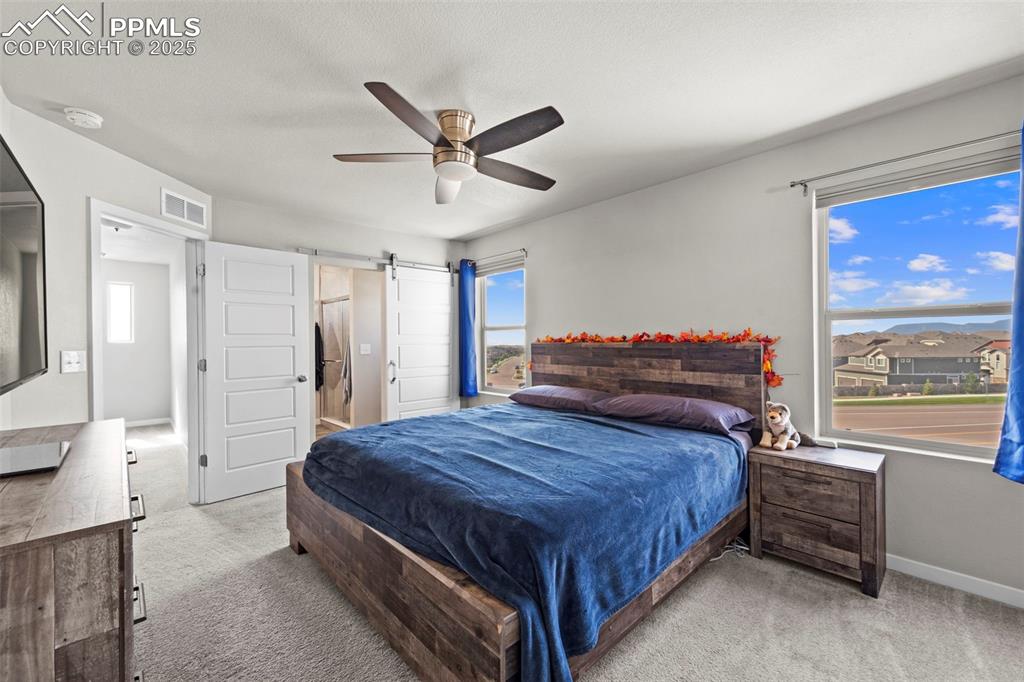 Image 17 of 30: Bedroom with a barn door, light carpet, and a ceiling fan