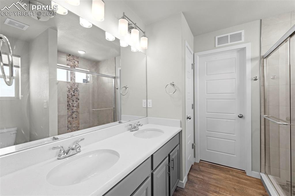 Image 18 of 30: Full bath featuring double vanity, a shower stall, and dark wood finished f
