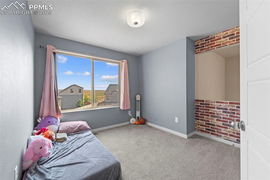 Image 22 of 30: Carpeted bedroom with baseboards and brick wall