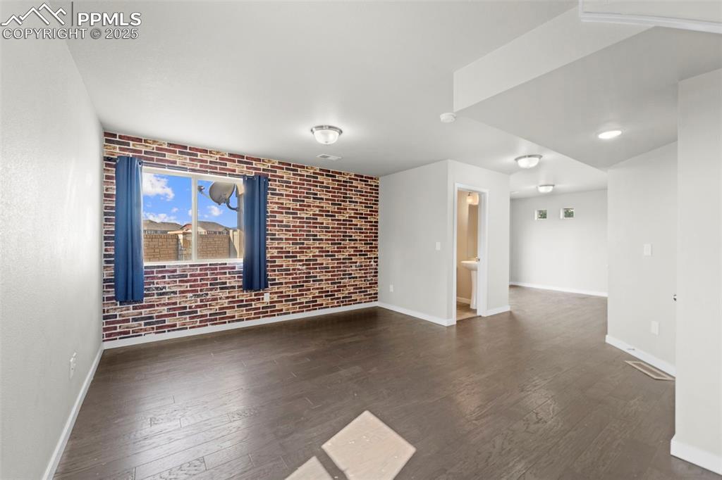 Image 23 of 30: Empty room with dark wood finished floors and brick wall