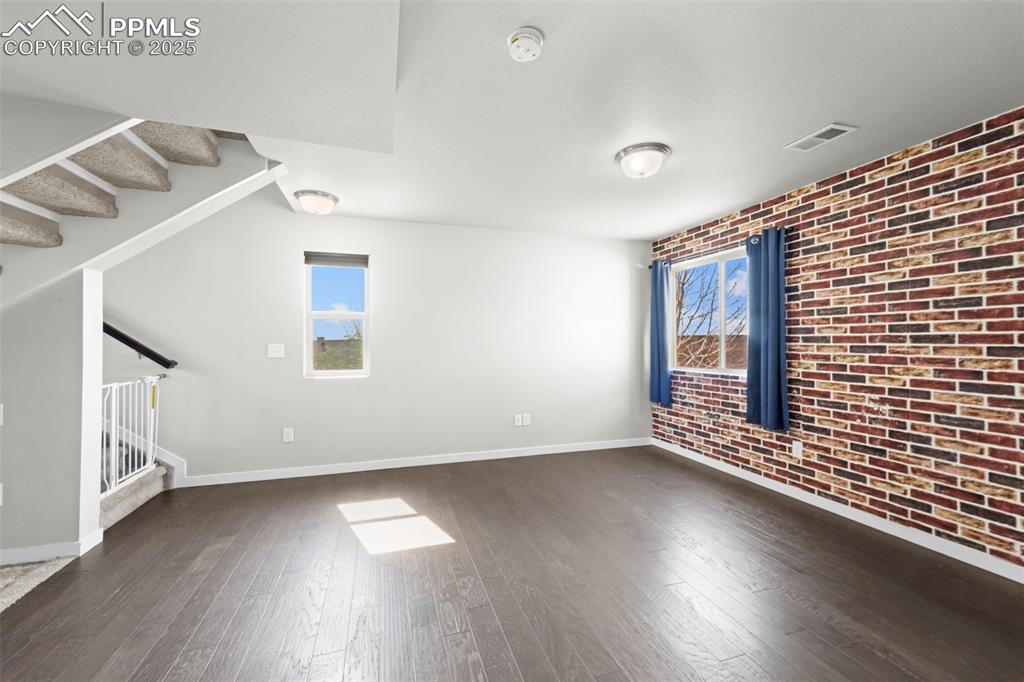Image 25 of 30: Unfurnished room with brick wall, dark wood-style flooring, and stairs