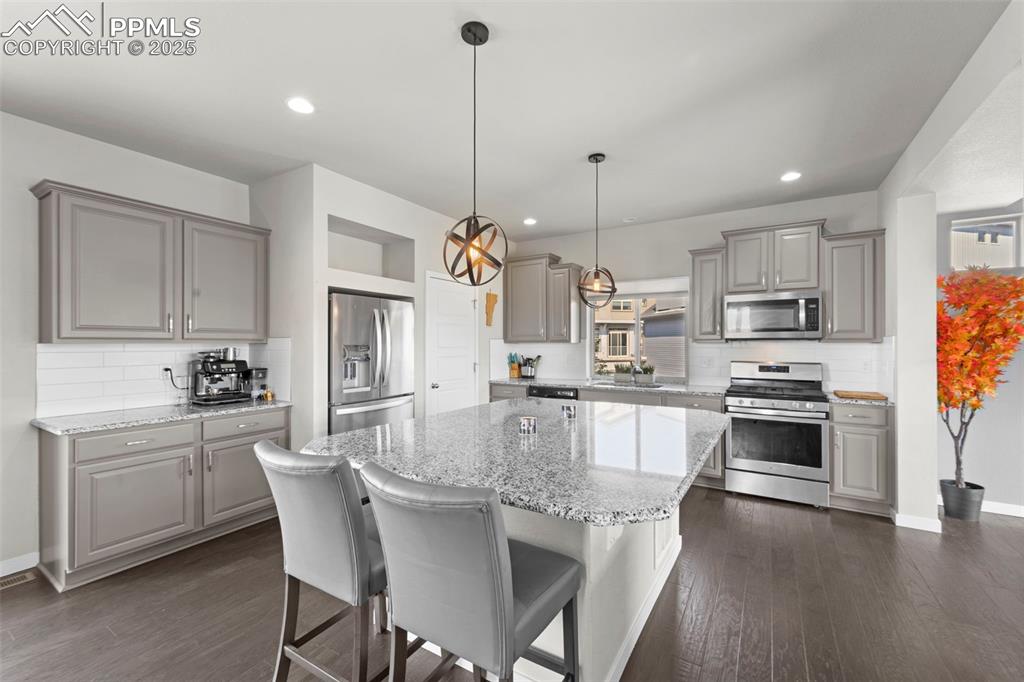Image 8 of 30: Kitchen with gray cabinets, decorative backsplash, appliances with stainles