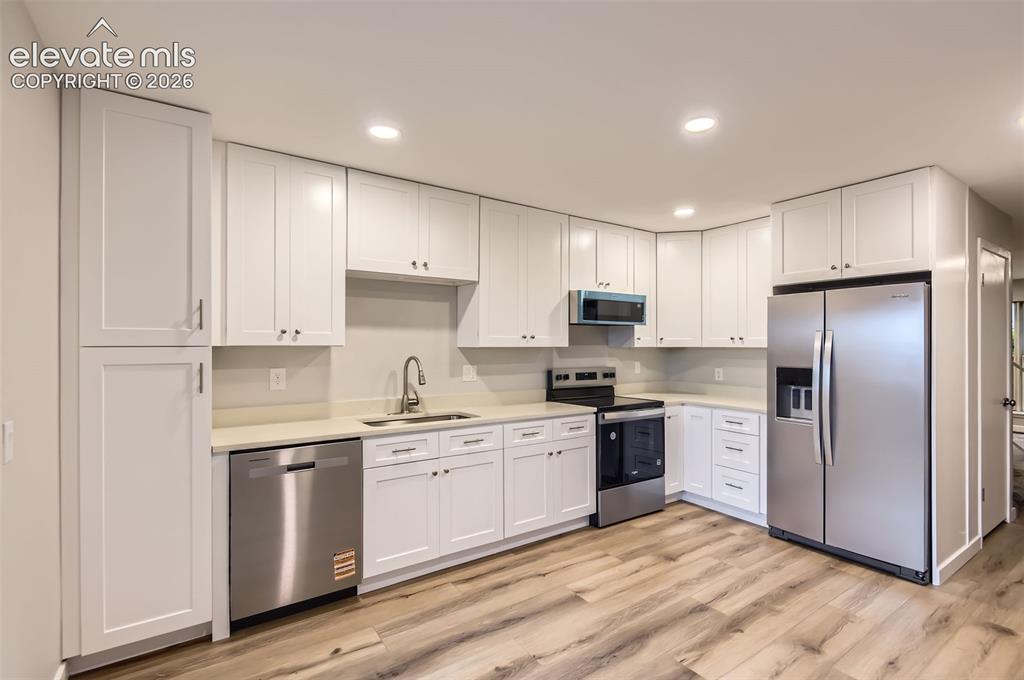 Image 10 of 32: Modern kitchen featuring extensive white shaker cabinetry, light-toned coun
