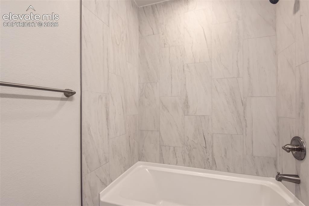 Image 21 of 32: White bathtub with an integrated shower, surrounded by light-toned, large-f