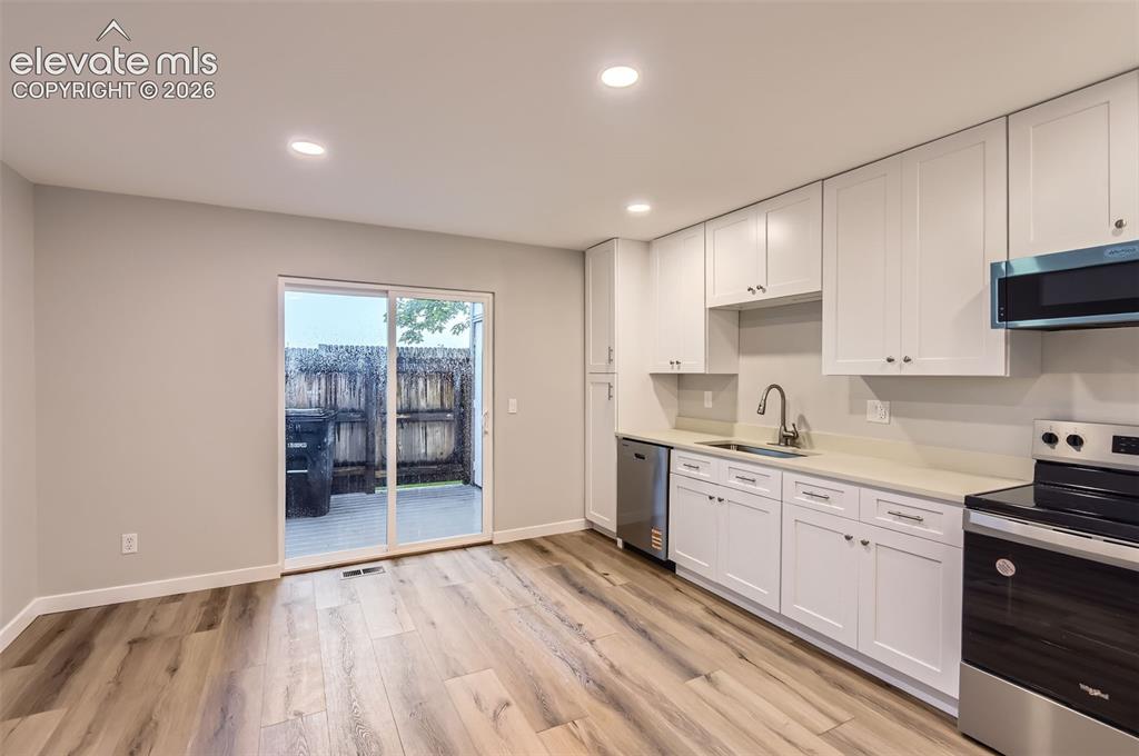 Image 8 of 32: Open-concept kitchen featuring white shaker-style cabinetry, light-toned co