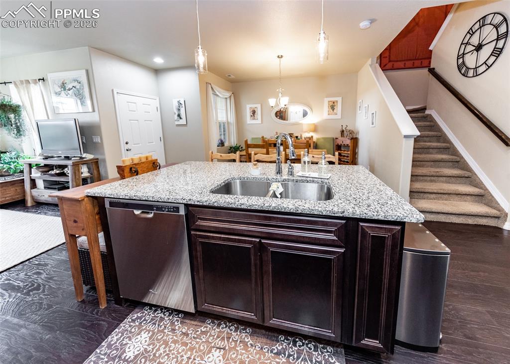 Image 15 of 32: Kitchen with dark brown cabinetry, stainless steel dishwasher, light stone 