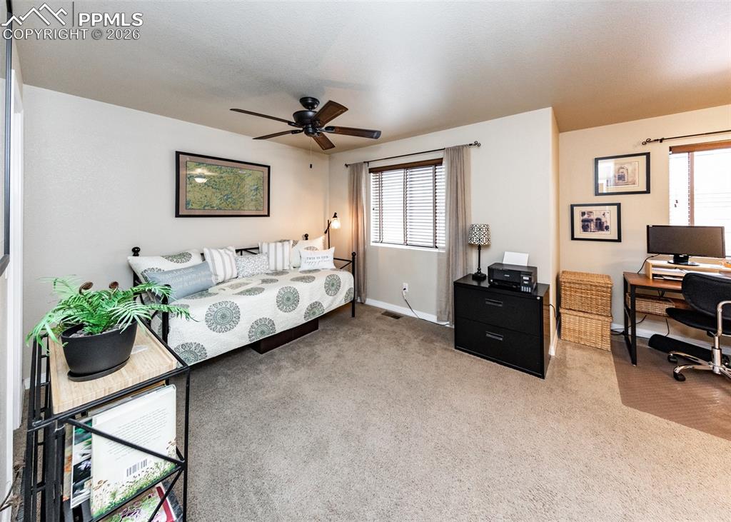 Image 23 of 32: Bedroom with light colored carpet, multiple windows, a desk, and ceiling fa