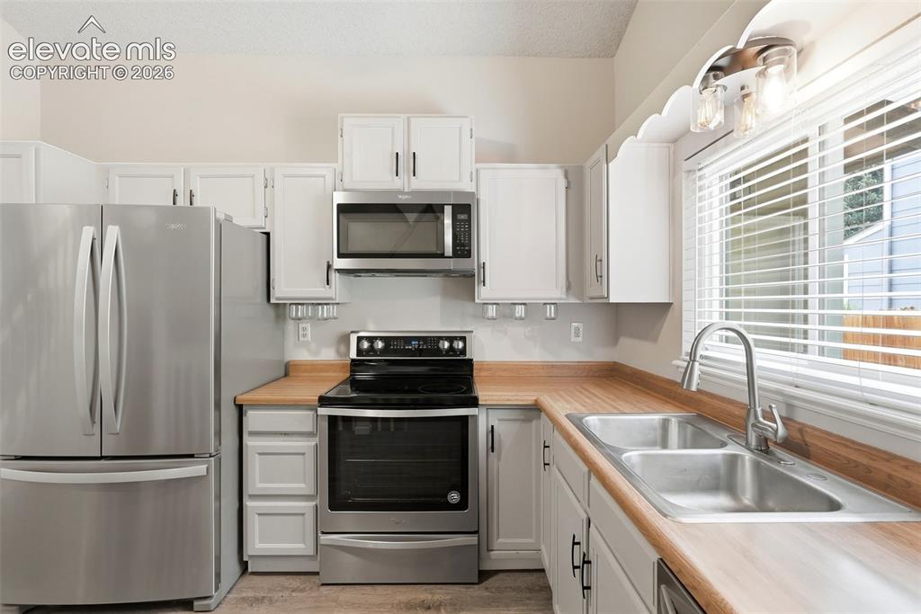 Image 10 of 35: Kitchen featuring stainless steel appliances, white cabinetry, wood-finish