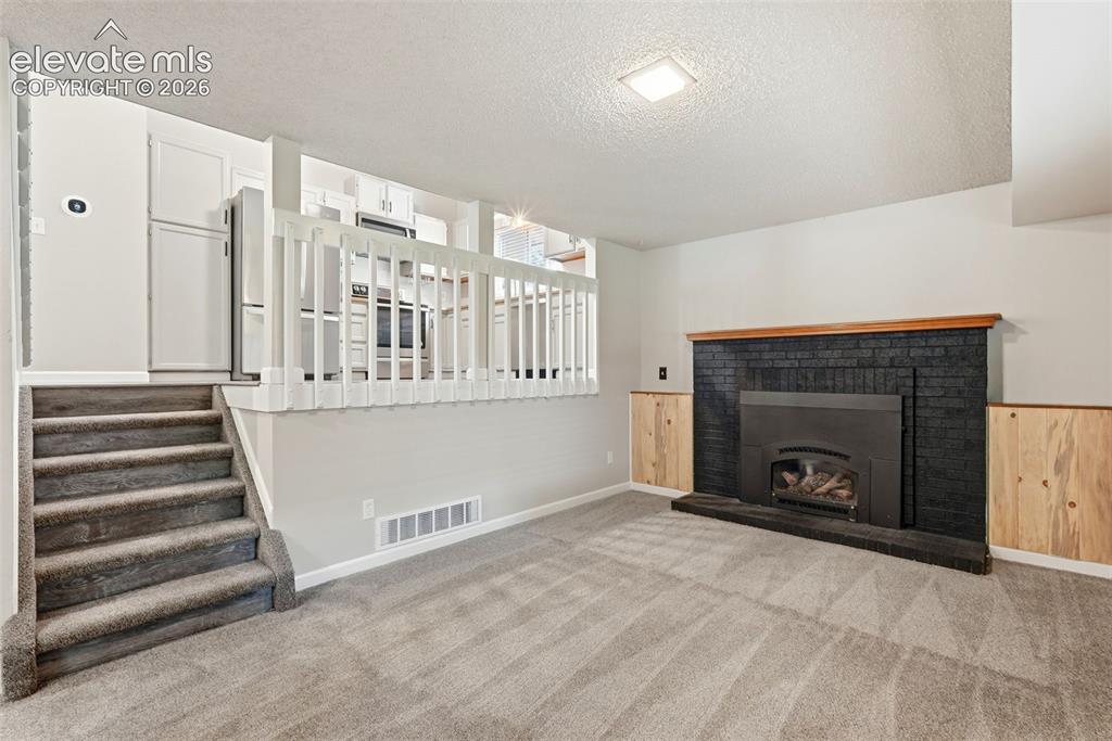Image 14 of 35: Lower-level living area featuring a black brick fireplace with a wood mantl