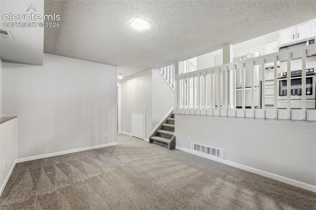 Image 16 of 35: Carpeted lower-level room featuring a half-wall partition with a white rail