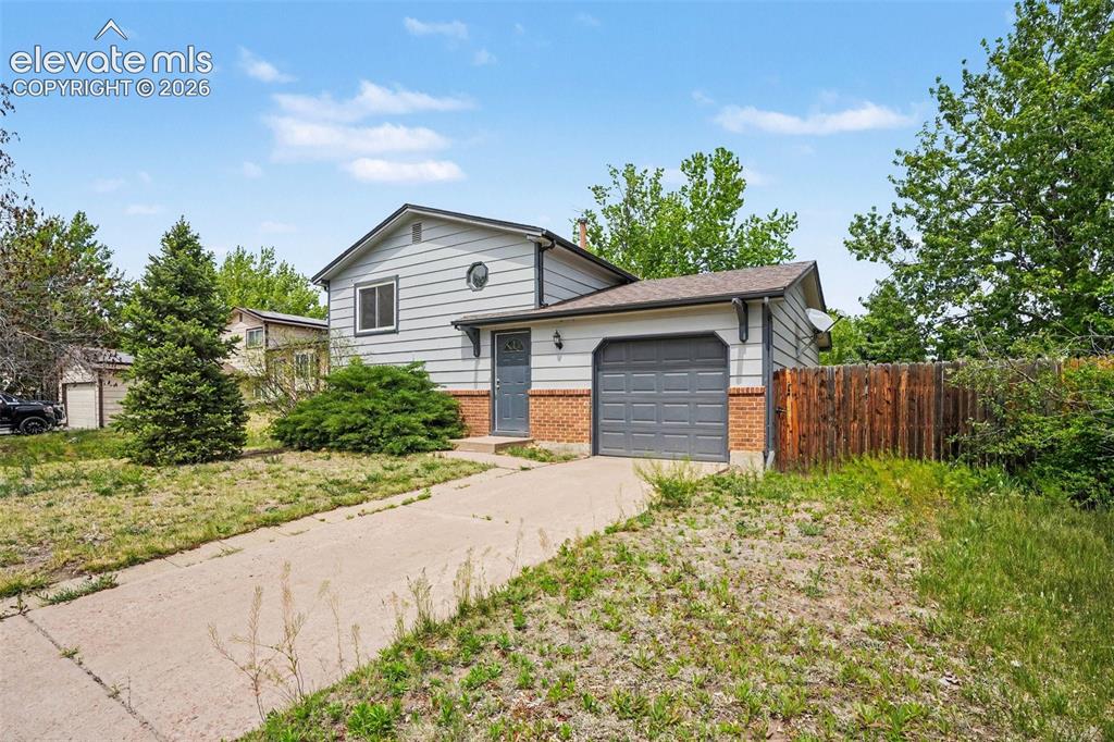 Caption: Split-level residence featuring light gray siding, a brick foundation, an attached one-car garage wi