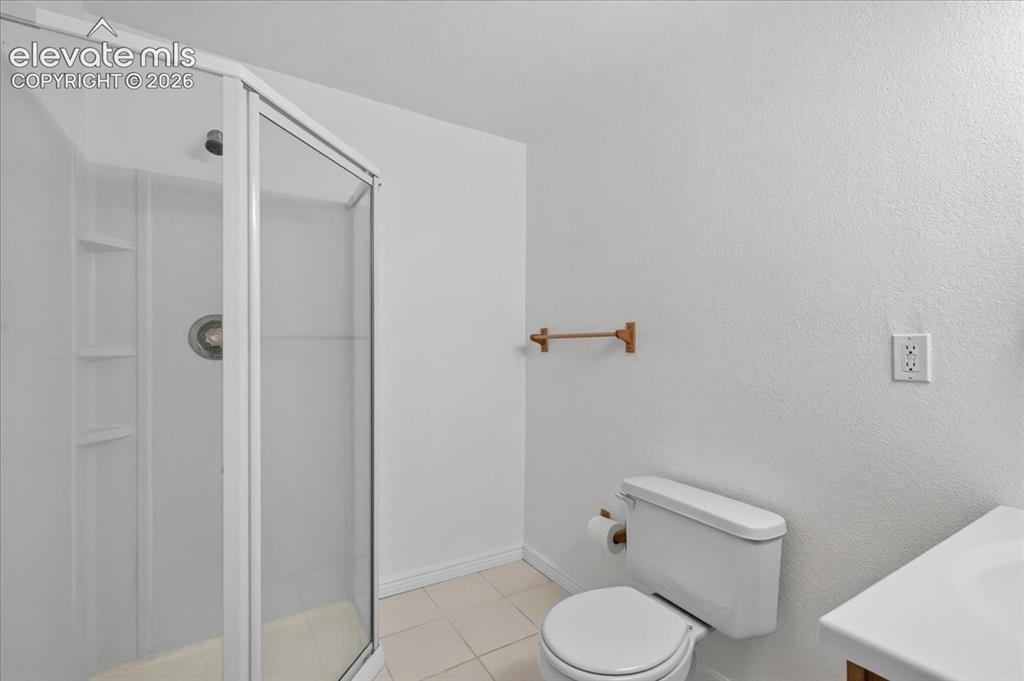 Image 28 of 44: Corner shower enclosure with built-in shelving, tile flooring, and a wall-m