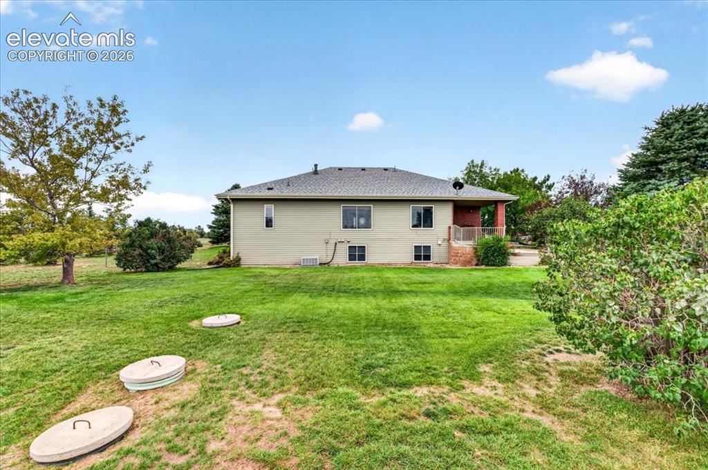 Image 32 of 44: Spacious backyard featuring a manicured lawn, mature trees, and a covered p