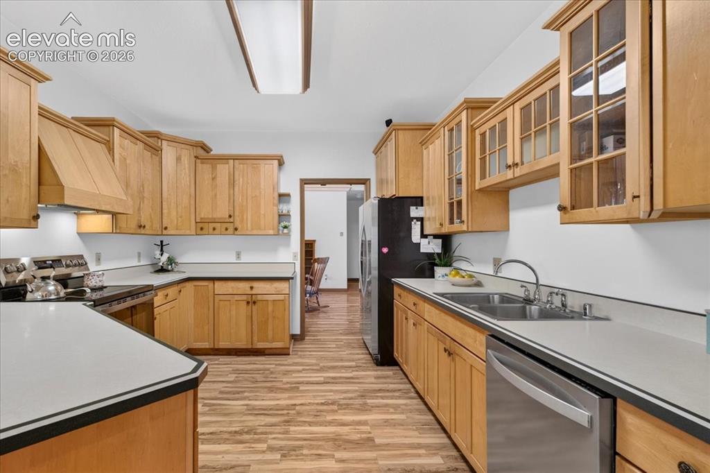 Image 8 of 44: Kitchen featuring natural wood cabinetry, glass-front upper cabinets, solid