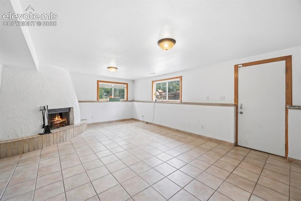 Image 12 of 20: Spacious room with tile flooring, a textured white stucco fireplace, and na