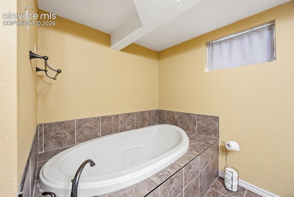Image 15 of 20: Built-in soaking tub with a dark tile surround and coordinating tile floori