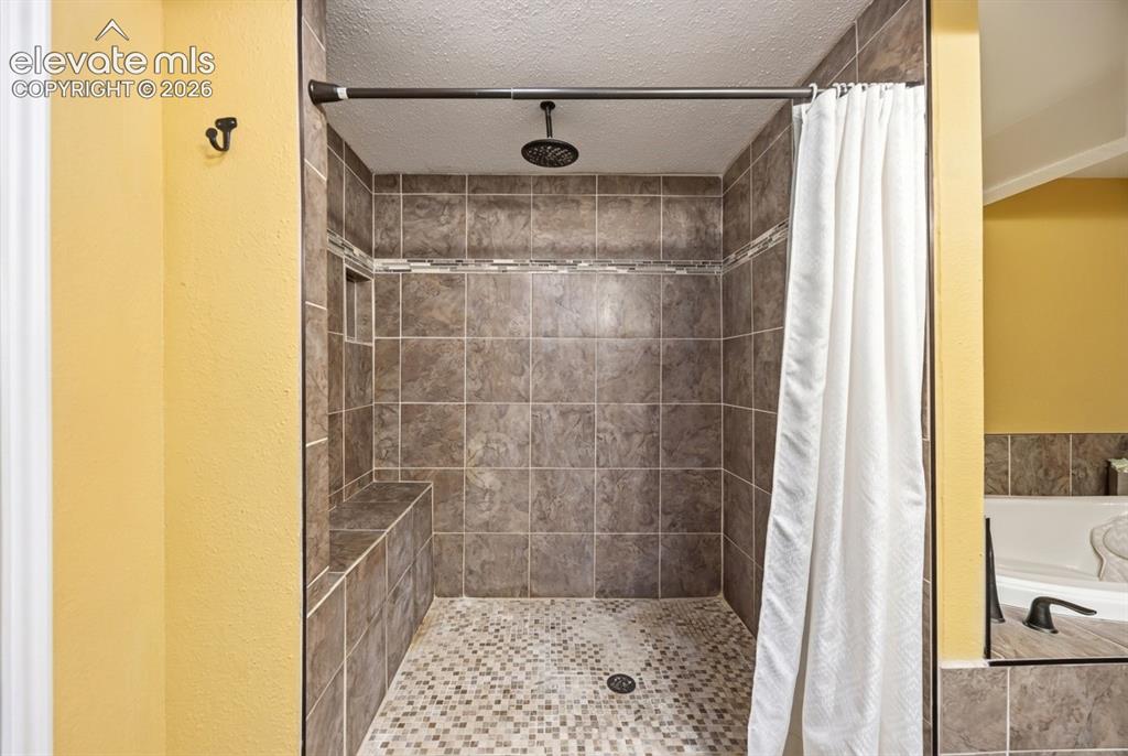 Image 17 of 20: Tiled shower enclosure featuring a built-in bench, recessed shelf, and mosa