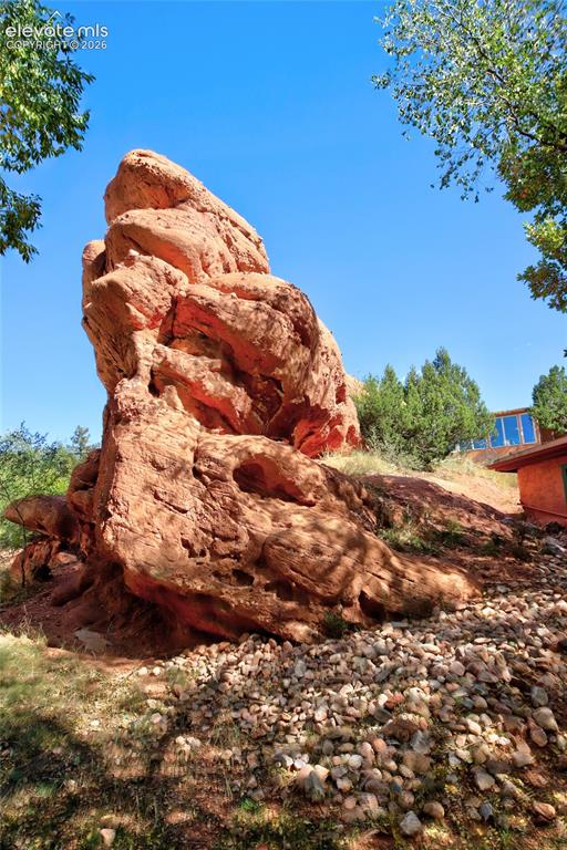 Image 13 of 26: Prominent natural red rock formation set against a landscape of mature tree