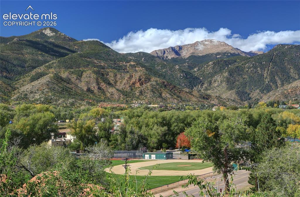 Image 15 of 26: Expansive mountain backdrop featuring mature trees and a baseball field
