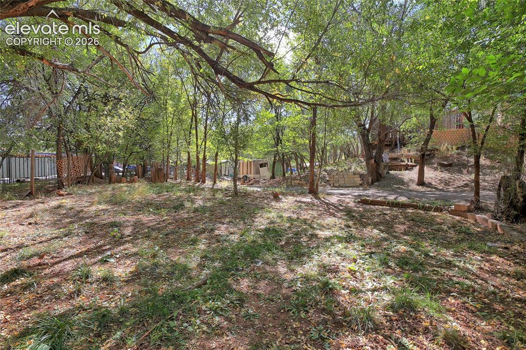 Image 17 of 26: Expansive lot featuring mature trees, natural terrain, and perimeter fencin