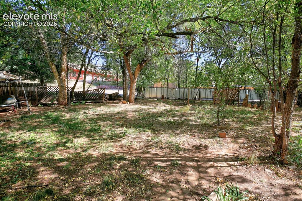 Image 18 of 26: Backyard featuring mature trees, partial wood lattice fencing, and a metal