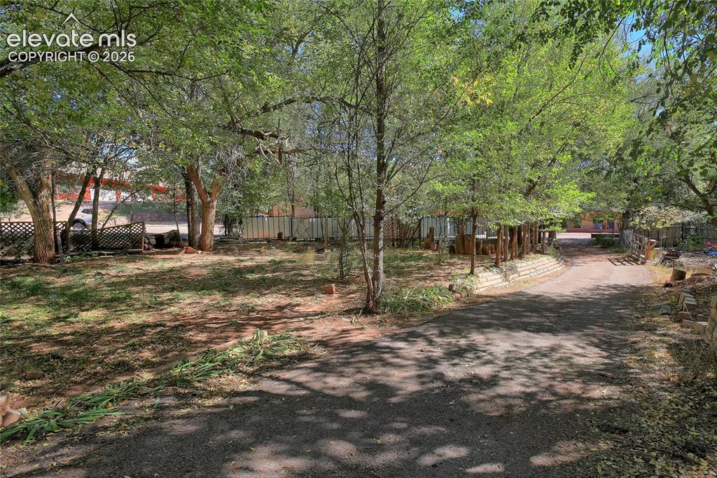 Image 19 of 26: Expansive grounds featuring a paved driveway, mature trees, tiered retainin