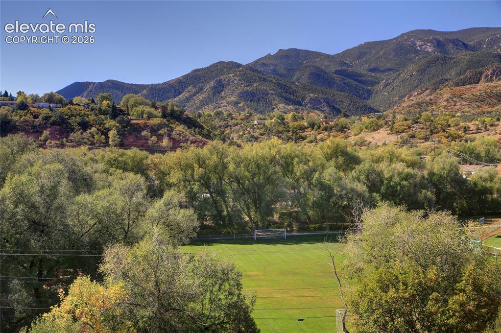 Image 9 of 26: Expansive green space featuring a soccer goal, mature trees, and a mountain
