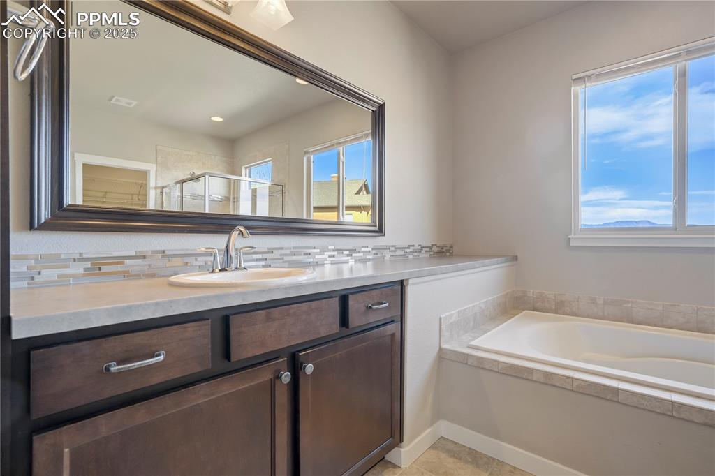 Image 23 of 50: Primary bath featuring vanity, backsplash, a garden tub, a shower stall, an